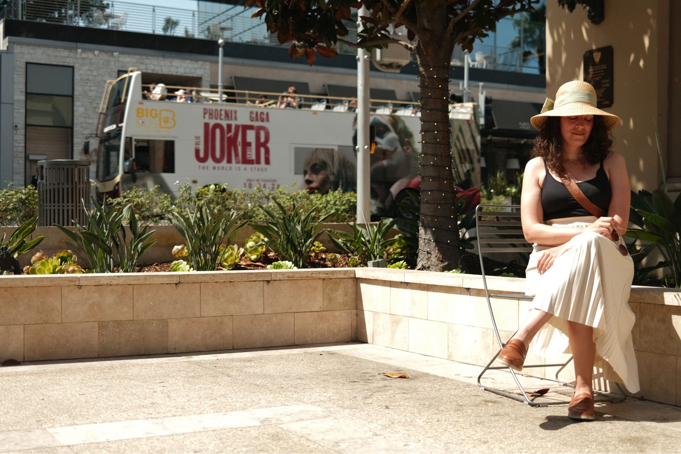 Frau mit Sonnenhut sitzt vor einem Tourbus mit Joker-Werbung in Hollywood